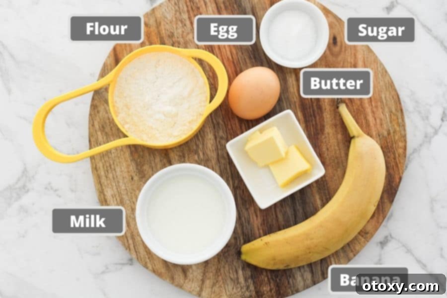 A rustic wooden board displays all the essential ingredients for banana pikelets: a ripe banana, an egg, a carton of milk, a bowl of flour, and a small container of sugar, ready for mixing.