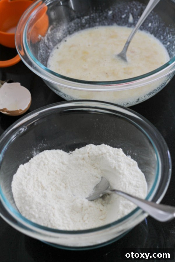 Two glass bowls on a kitchen counter: one contains mashed banana mixed with egg and milk, and the other holds a blend of self-raising flour and sugar, preparing for the next step of the recipe.