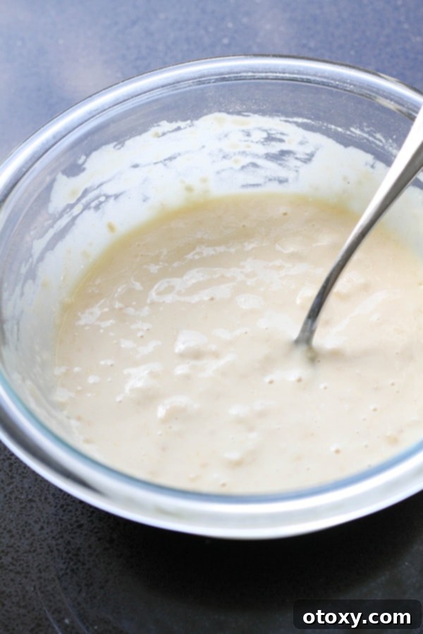 A glass bowl filled with a smooth, golden-yellow banana pikelet batter, ready to be cooked. The consistency appears thick yet easily pourable.