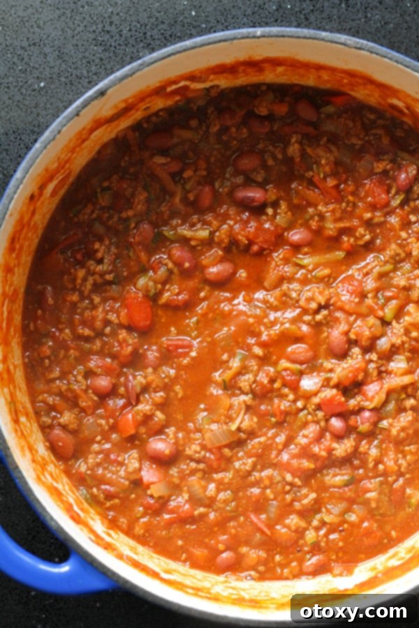 A large, steaming pot of healthy Chilli Con Carne, rich in color and texture, bubbling gently on a stovetop.