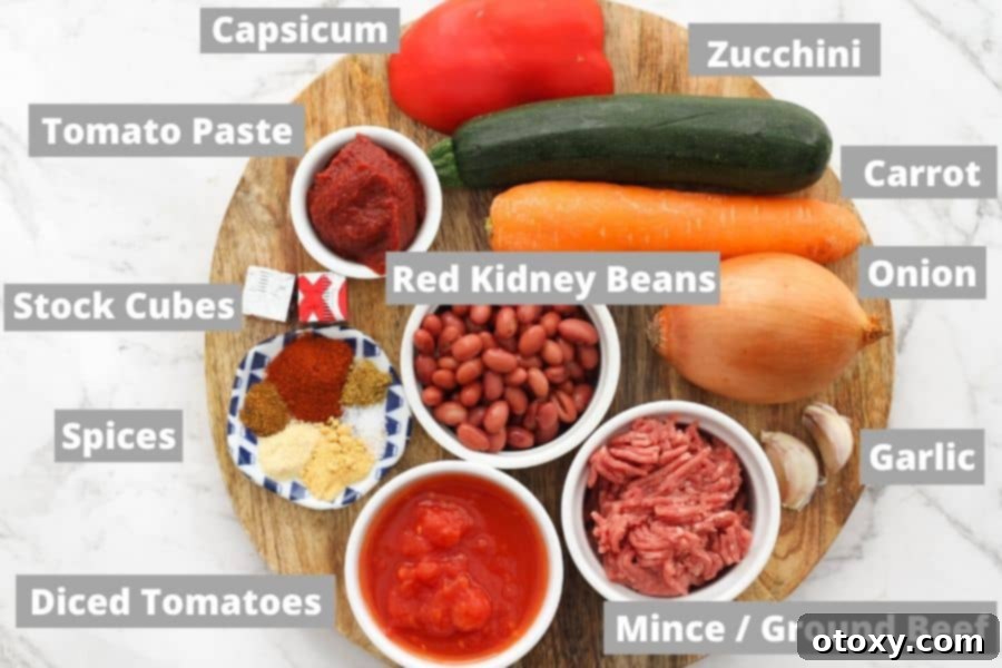 A neatly arranged collection of fresh ingredients for Chilli Con Carne, including diced vegetables, spices, and canned goods, laid out on a rustic wooden board.