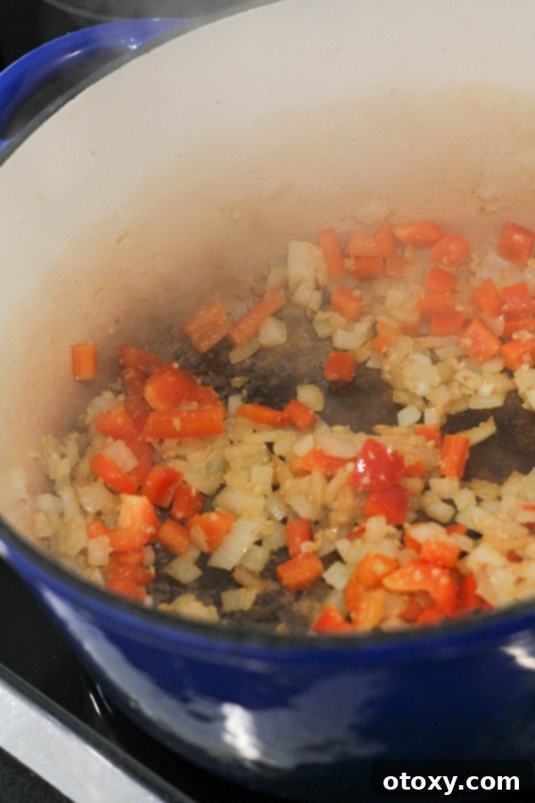 Diced onion and capsicum (bell pepper) gently cooking in olive oil within a large pot, beginning to soften and release their aromas.