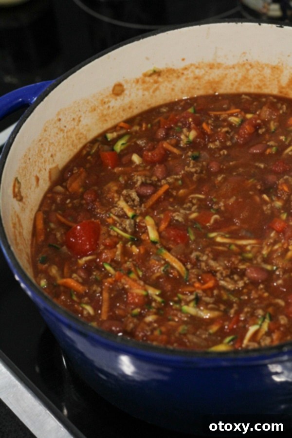 A rich, red chilli con carne mixture simmering gently in a large pot, with visible vegetables and beans, concentrating its flavours.