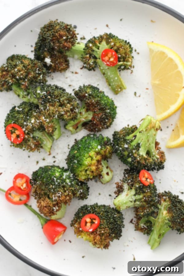 roasted broccoli on a white plate with lemon wedges and chopped chilli.