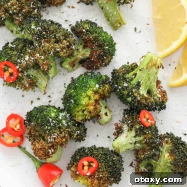 roasted broccoli on a white plate with lemon wedges and chopped chilli.