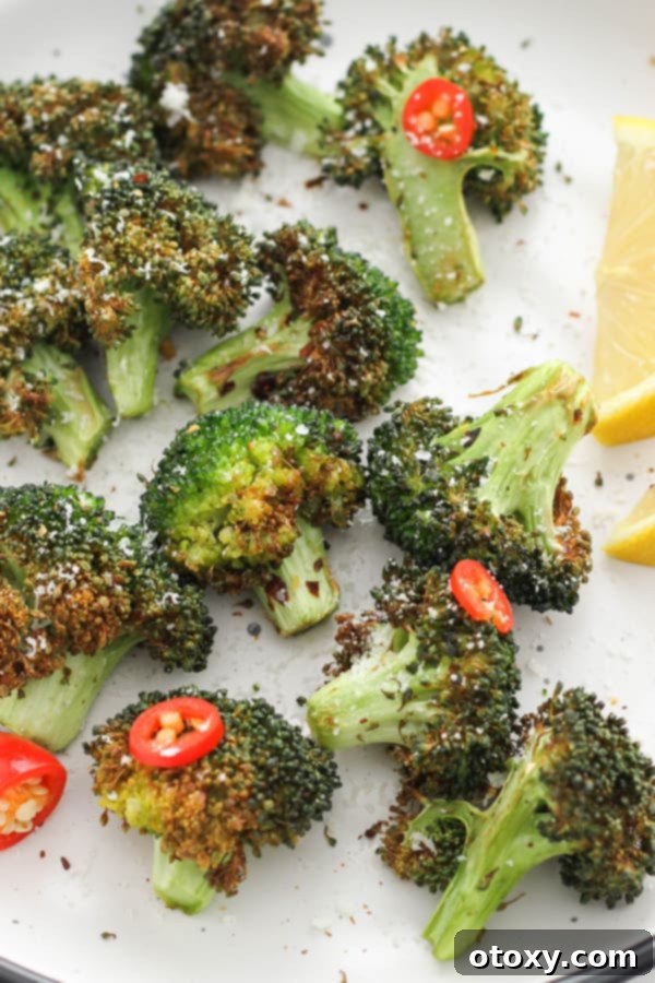 roasted broccoli on a white plate with lemon wedges and chopped chilli.