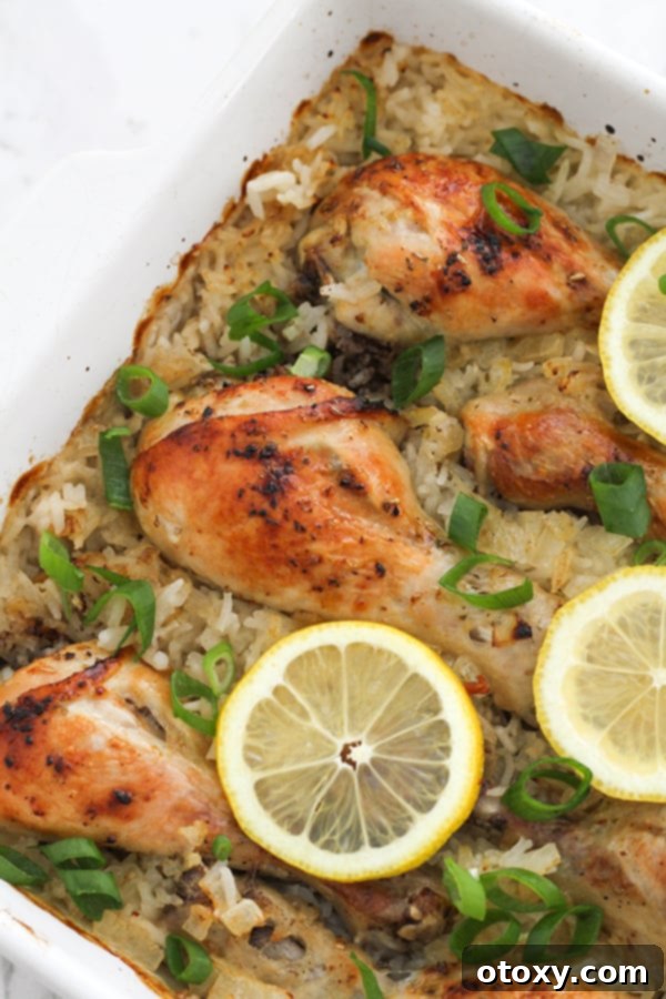 Close-up shot of golden-brown chicken drumsticks resting on a bed of lemon-infused rice in a white baking dish, garnished with fresh lemon slices and parsley.