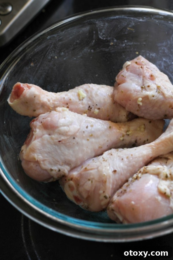 Raw chicken drumsticks are shown marinating in a glass bowl with lemon, garlic, and oregano, ready for the oven.