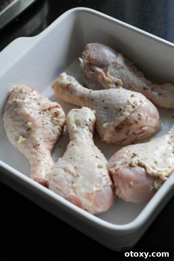 Partially cooked chicken drumsticks are spread in a single layer in a baking dish, browning slightly in the oven.