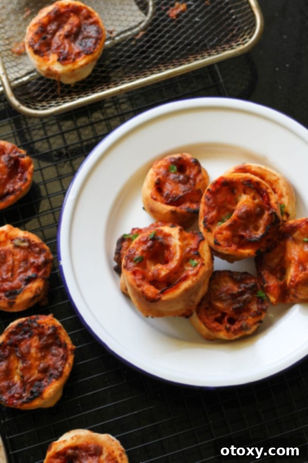 Golden brown Air Fryer Pizza Pinwheels piled high on a pristine white plate, garnished with fresh herbs.