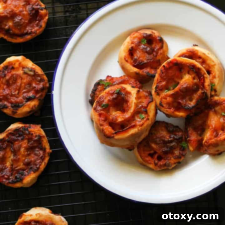 Golden brown Air Fryer Pizza Pinwheels piled high on a pristine white plate, garnished with fresh herbs.