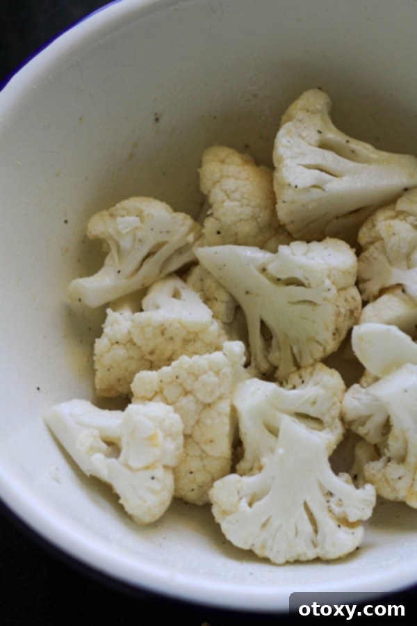 Cauliflower florets seasoned with olive oil and spices in a white mixing bowl, ready for the air fryer.