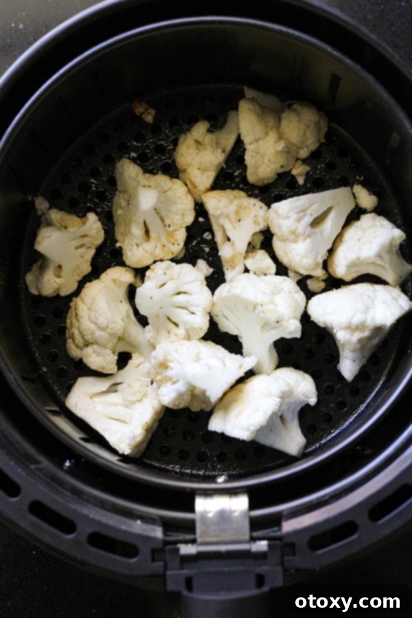 Seasoned cauliflower florets arranged in a single layer within an air fryer basket, ready for cooking.
