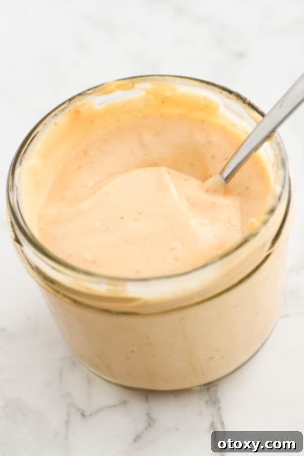 sriracha aioli in a glass jar with a spoon stuck inside.