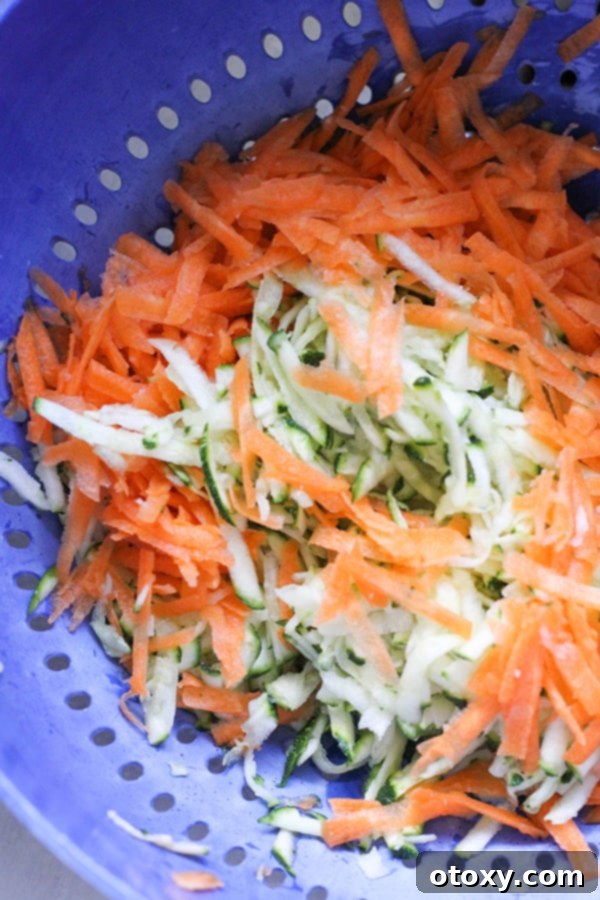 Golden Garden Fritters 5 Salted and shredded zucchini and carrot draining in a colander in the sink.