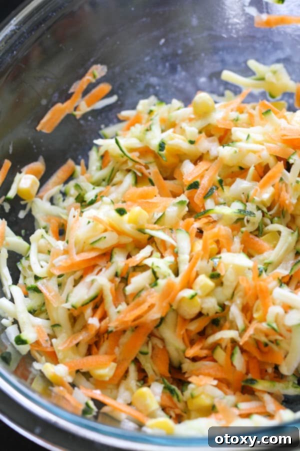 Golden Garden Fritters 6 Shredded zucchini and carrot in a glass mixing bowl with added egg, corn, onion, cheese, salt, and pepper.