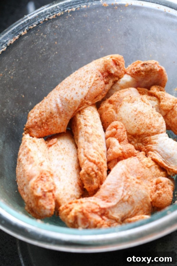Air-Fried Wing Perfection 7 A close-up view of seasoned raw chicken wings in a clear glass bowl, showcasing their even coating of spices.