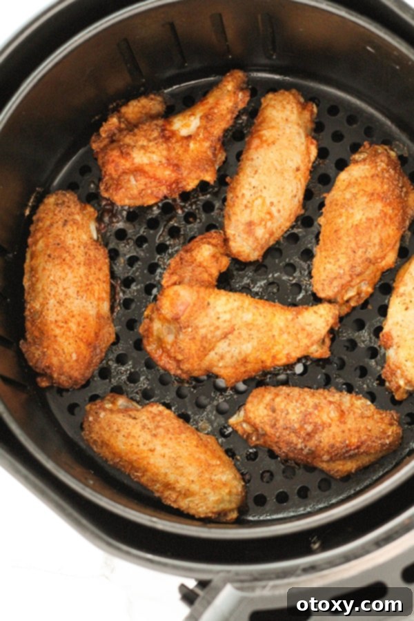 Air-Fried Wing Perfection 9 Crispy, golden-brown cooked chicken wings are nestled in an air fryer basket, looking perfectly done.