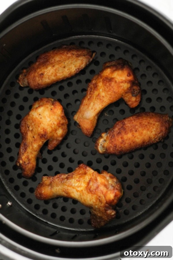 Air-Fried Wing Perfection 10 Hot and crispy cooked chicken wings, glistening with a fresh coat of buffalo sauce, are arranged in an air fryer basket.