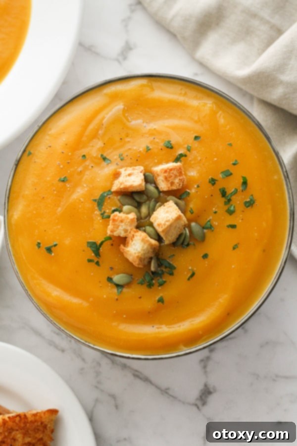 A generous serving of creamy pumpkin soup, elegantly topped with golden croutons and green pumpkin seeds, invitingly arranged in a white bowl.