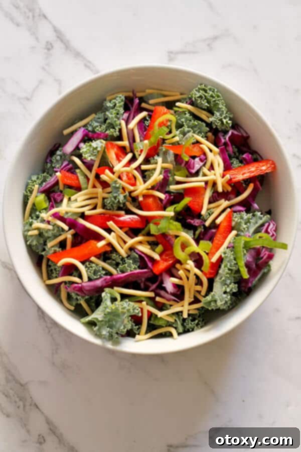 A close-up shot of the vibrant crunchy kale salad with lemon tamari dressing in a clean white bowl, highlighting the textures and colors of the fresh ingredients.