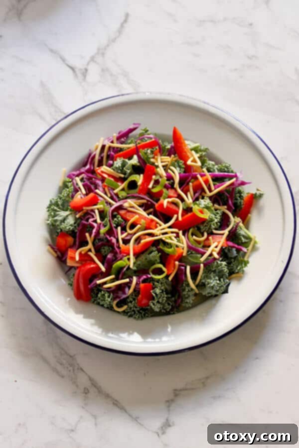 A vibrant portion of crunchy kale salad with lemon tamari dressing served on a white plate, ready to be enjoyed.