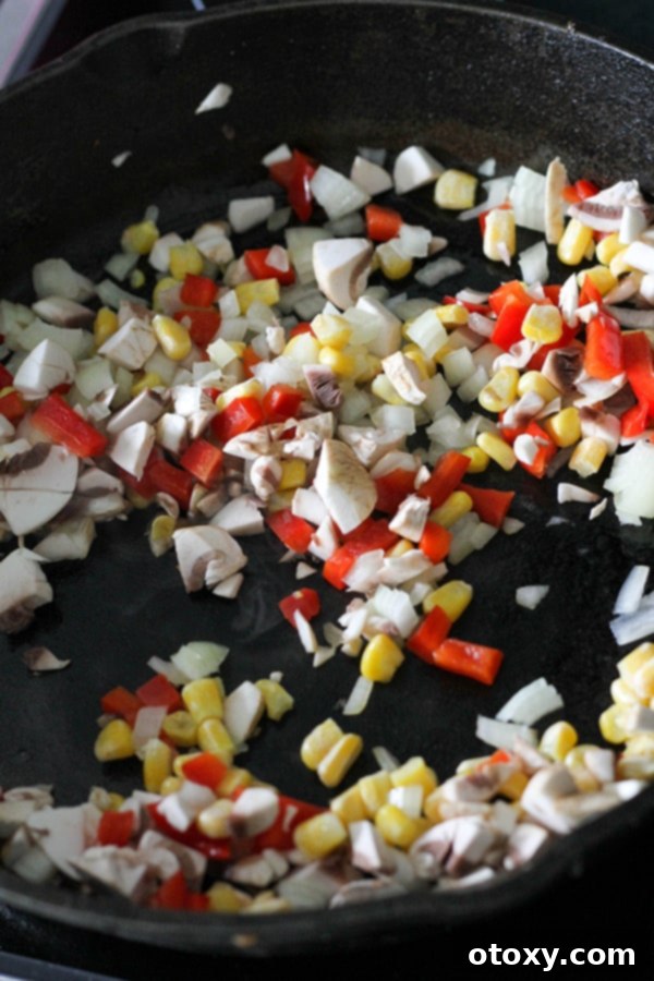 Finely diced onions, bell peppers, mushrooms, and corn sizzling gently in a cast iron pan.