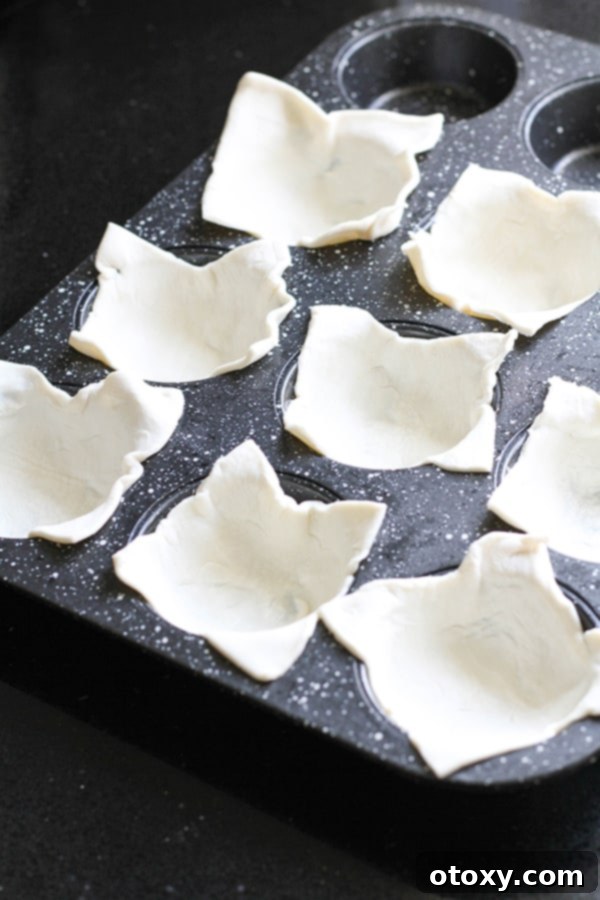Puff pastry squares carefully pressed into each cup of a muffin tin, ready for filling.
