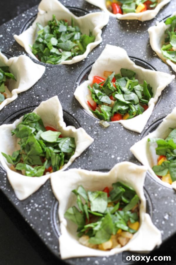 Puff pastry cases filled with a colorful medley of sautéed vegetables and fresh spinach, ready for the egg mixture.