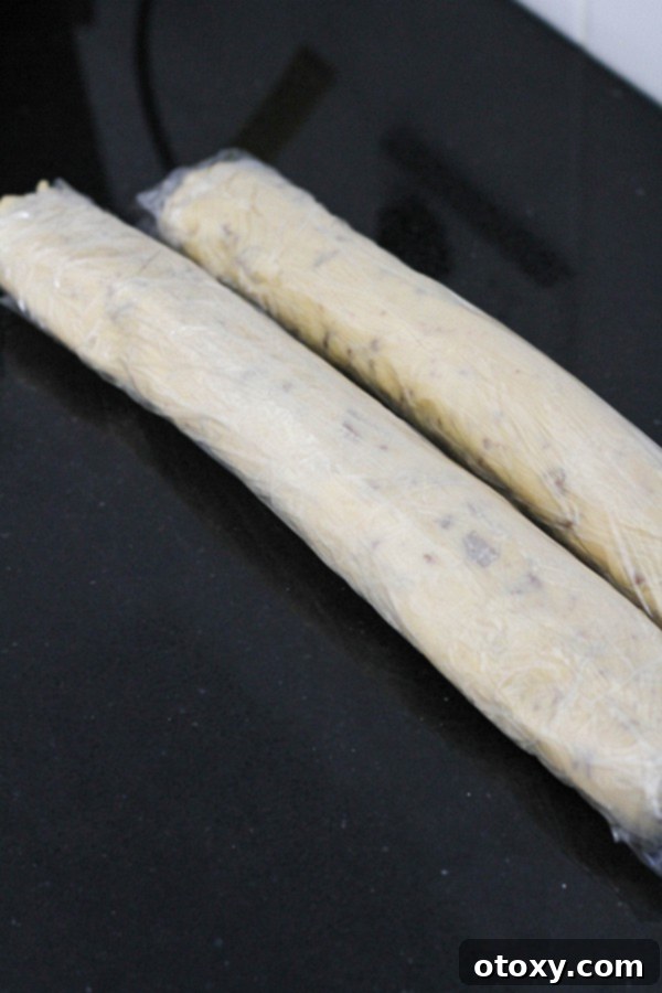 Shortbread cookie dough expertly rolled into a log and secured in plastic wrap, ready for chilling.