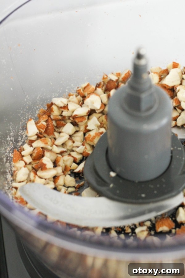 Tropical Date Energy Bites 5 Roughly chopped almonds inside a food processor bowl, showing the perfect texture before adding other ingredients.