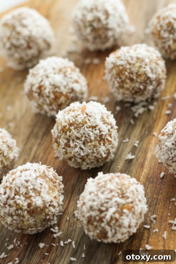 Tropical Date Energy Bites 8 Freshly rolled coconut date balls, coated in coconut, resting on a rustic wooden board.