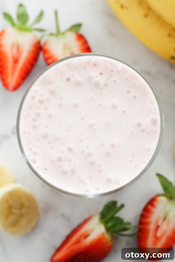 Smoothie in a glass surrounded by fresh strawberries and banana slices, highlighting natural ingredients.