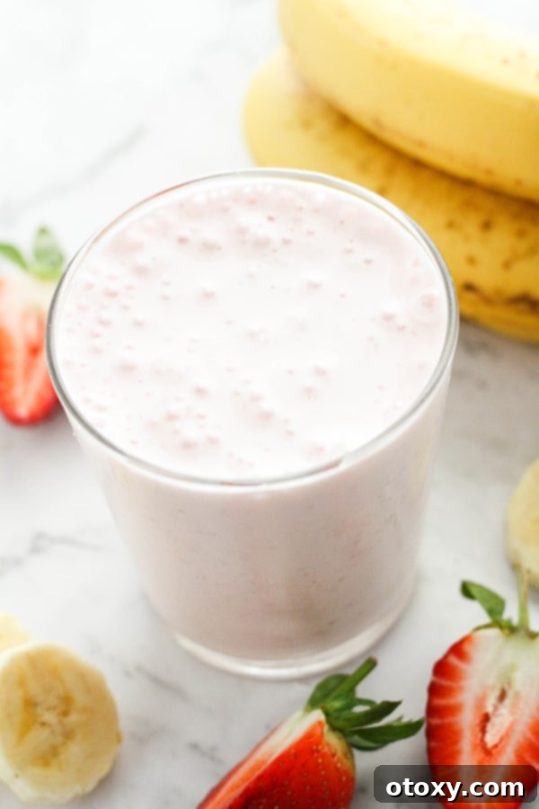 Close-up of a strawberry yogurt smoothie in a clear glass, with fresh strawberries and banana slices artfully arranged around it.