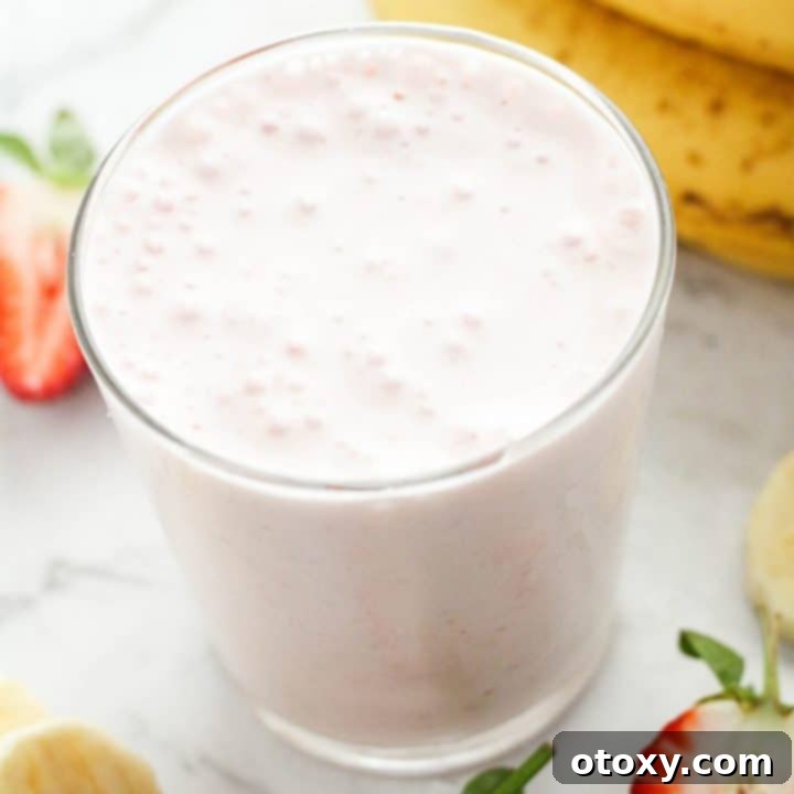 Strawberry smoothie in a glass surrounded by strawberries and banana slices, showcasing the final product.