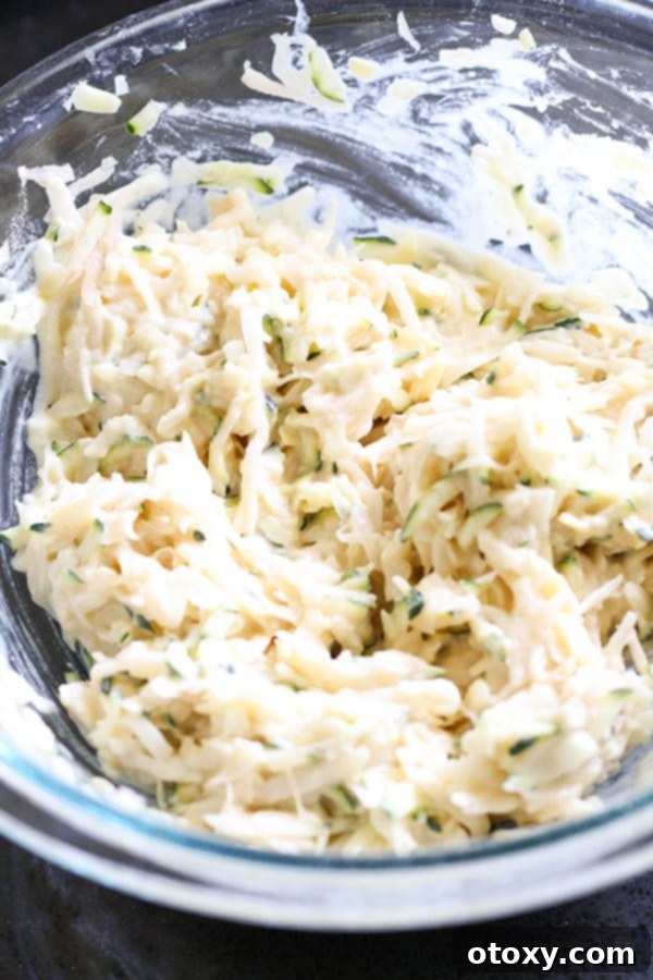 A close-up shot of the mixed fritter batter in a clear glass bowl, showcasing its thick and chunky texture, ready for frying.
