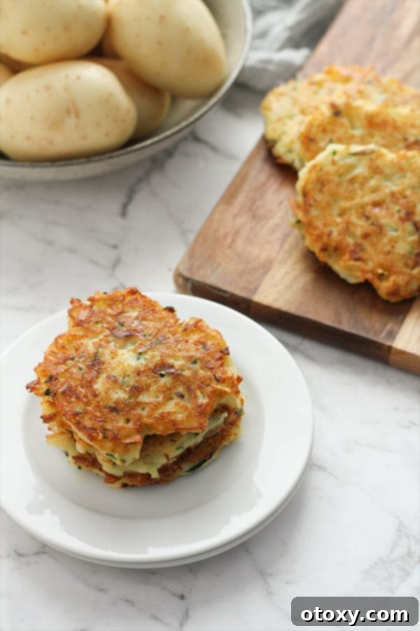 A stack of potato fritters sits on a plate, with blurred fresh potatoes in a bowl in the background, emphasizing the ingredient and the finished product.