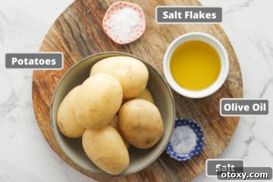 A rustic wooden board displaying the minimal yet essential ingredients for glass potatoes: whole potatoes, a bottle of olive oil, and two types of salt.