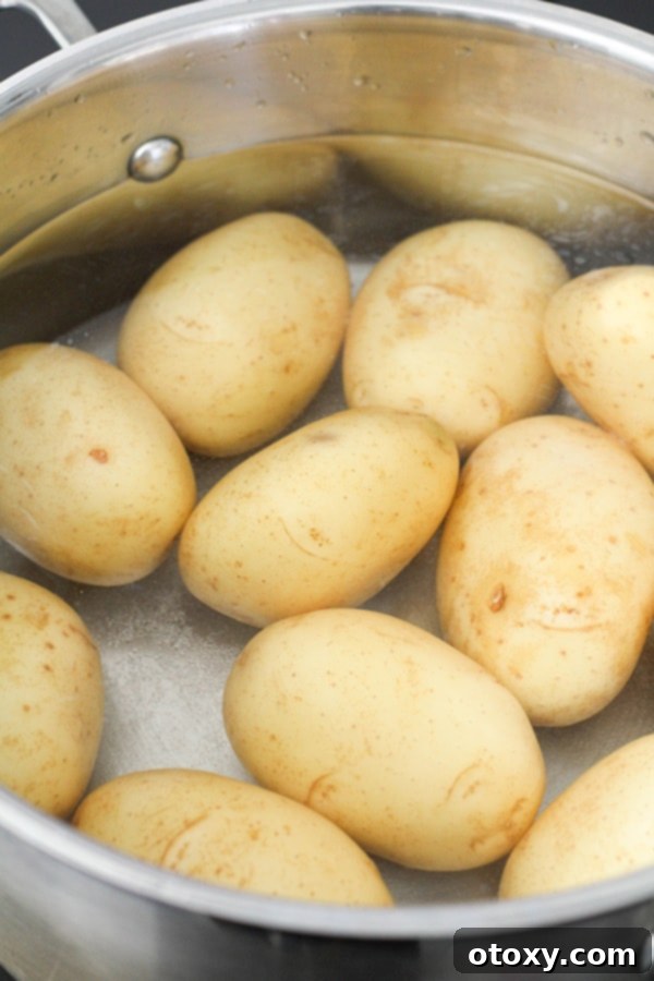 Whole potatoes boiling in a large pot on a stovetop, their skins beginning to soften and split.
