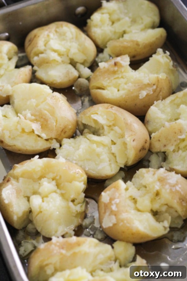 Smashed potatoes, glistening with olive oil and sprinkled with salt flakes, arranged in a roasting pan before cooking.