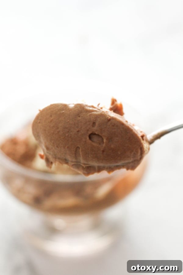 A spoon delicately scooping a generous portion of creamy chocolate mousse from a serving cup, showcasing its light and airy texture.