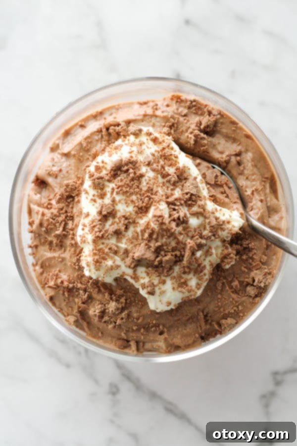 A serving of elegant chocolate mousse in a glass, topped with a swirl of whipped cream and delicate grated chocolate.