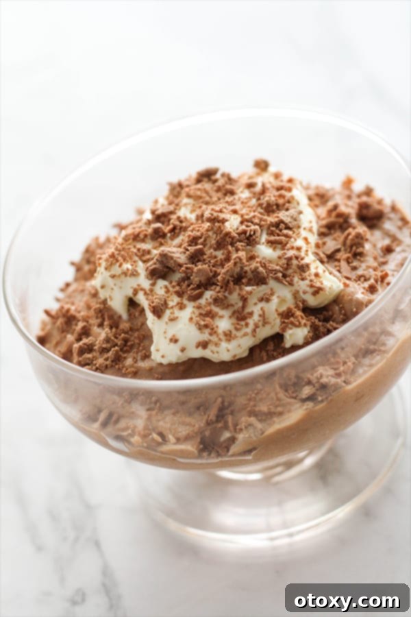A close-up shot of a glass filled with two-ingredient chocolate mousse, garnished with a generous dollop of whipped cream and delicate chocolate shavings, highlighting its rich texture.