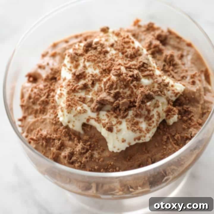 Rich chocolate mousse in a glass, elegantly topped with fluffy whipped cream and a sprinkle of grated chocolate, ready to be served.