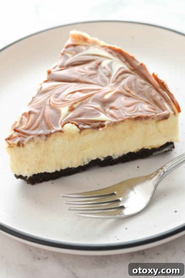 A perfectly sliced no-bake marble cheesecake, showing the beautiful chocolate swirl and Oreo crust, served on a white plate with a fork.