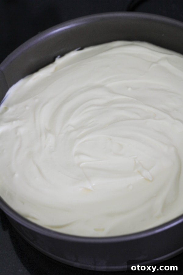 Creamy cheesecake mixture being poured over the Oreo crust in a springform pan.
