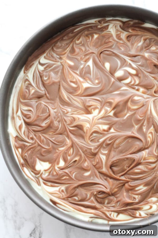 The stunning chocolate swirl being created on top of the smooth cheesecake mixture with a toothpick.