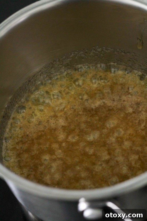 Butter, sugar, and cinnamon melting together in a saucepan, forming a bubbly glaze.