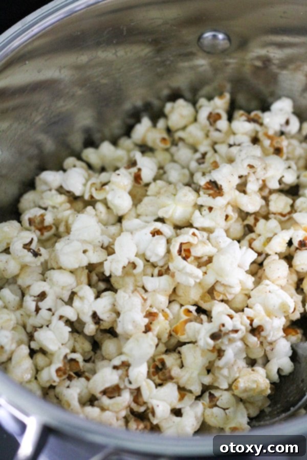 Popped popcorn in a saucepan, being coated with the sweet and buttery cinnamon sugar mixture.
