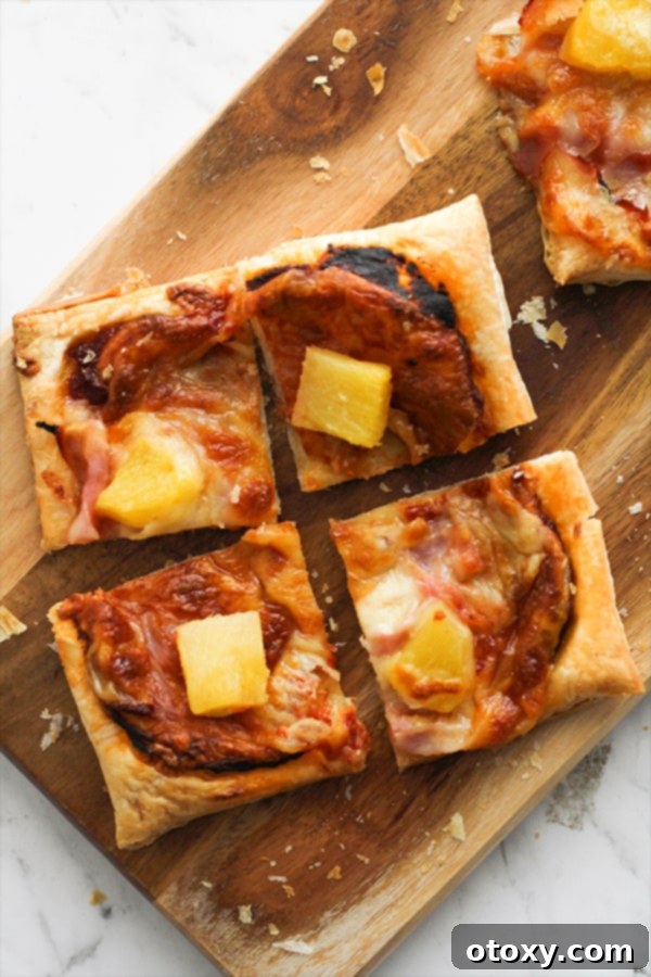 Slices of Hawaiian puff pastry pizza on a wooden serving board.